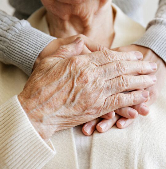 younger woman standing behind elder woman with her hands on her heart