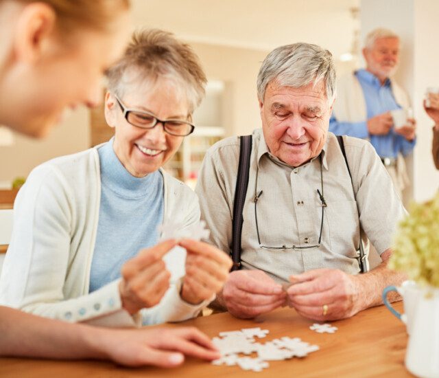 two seniors and a caregiver putting a puzzle together