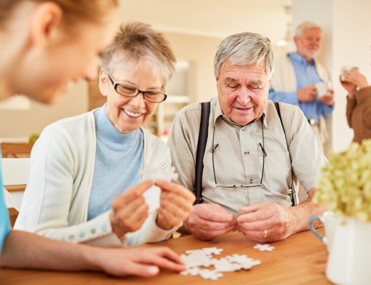 two seniors and a caregiver putting a puzzle together