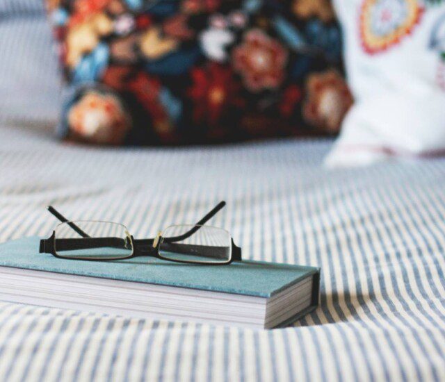 small book sitting on a bed with reading glass on top