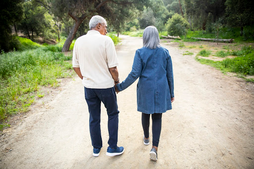 elder couple walking hand in hand down a dirt road