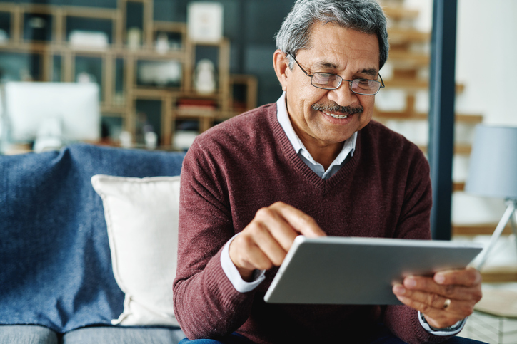 Cropped shot of a mature man using his digital tablet while relaxing at home