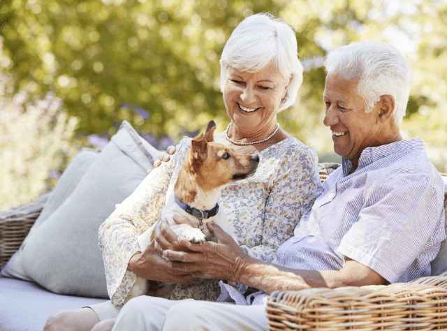 resident couple holding and petting their dog on a couch outside