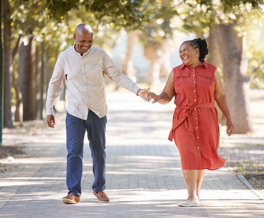 Happy affectionate mature african american couple walking and holding hands outside at the park during summer. In love seniors smiling hand in hand while spending quality time together outdoors