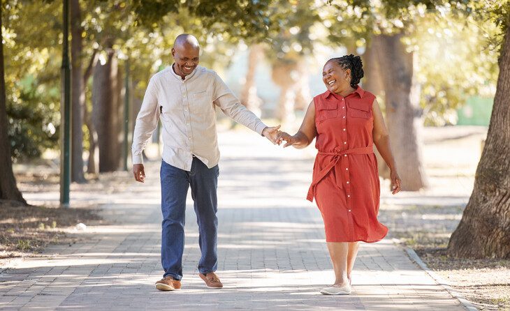 Happy affectionate mature african american couple walking and holding hands outside at the park during summer. In love seniors smiling hand in hand while spending quality time together outdoors