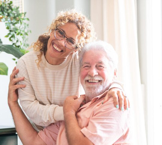 Portrait of happy middle-aged woman and senior father hugging spending time together at home