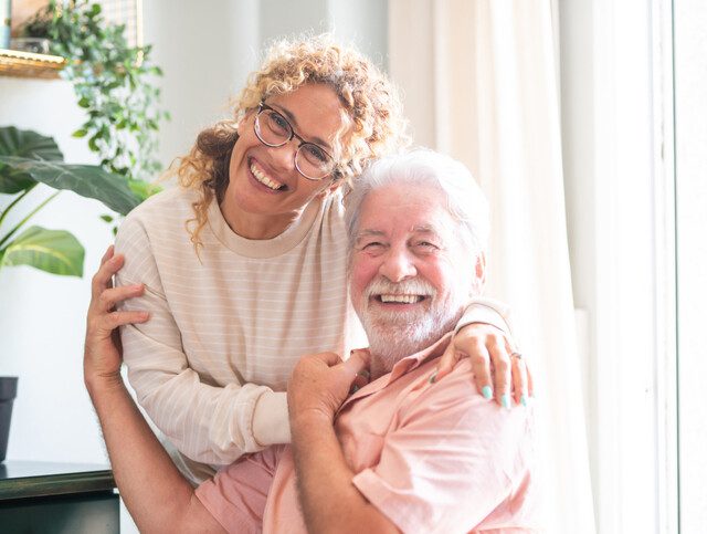 Portrait of happy middle-aged woman and senior father hugging spending time together at home