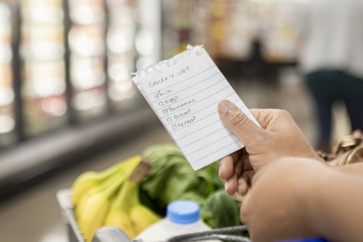hand holds up a grocery list while shopping at the store