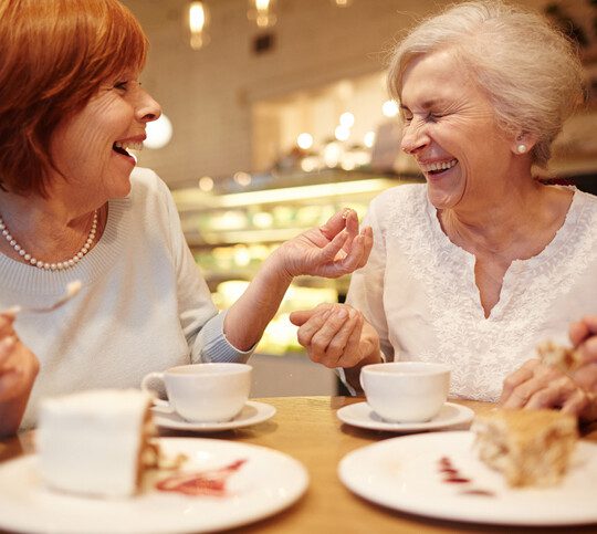 Two senior friendly females laughing during tea time