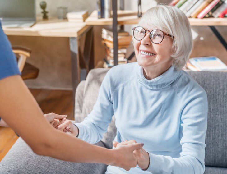 female resident looking up and smiling at caregiver while holding her hands