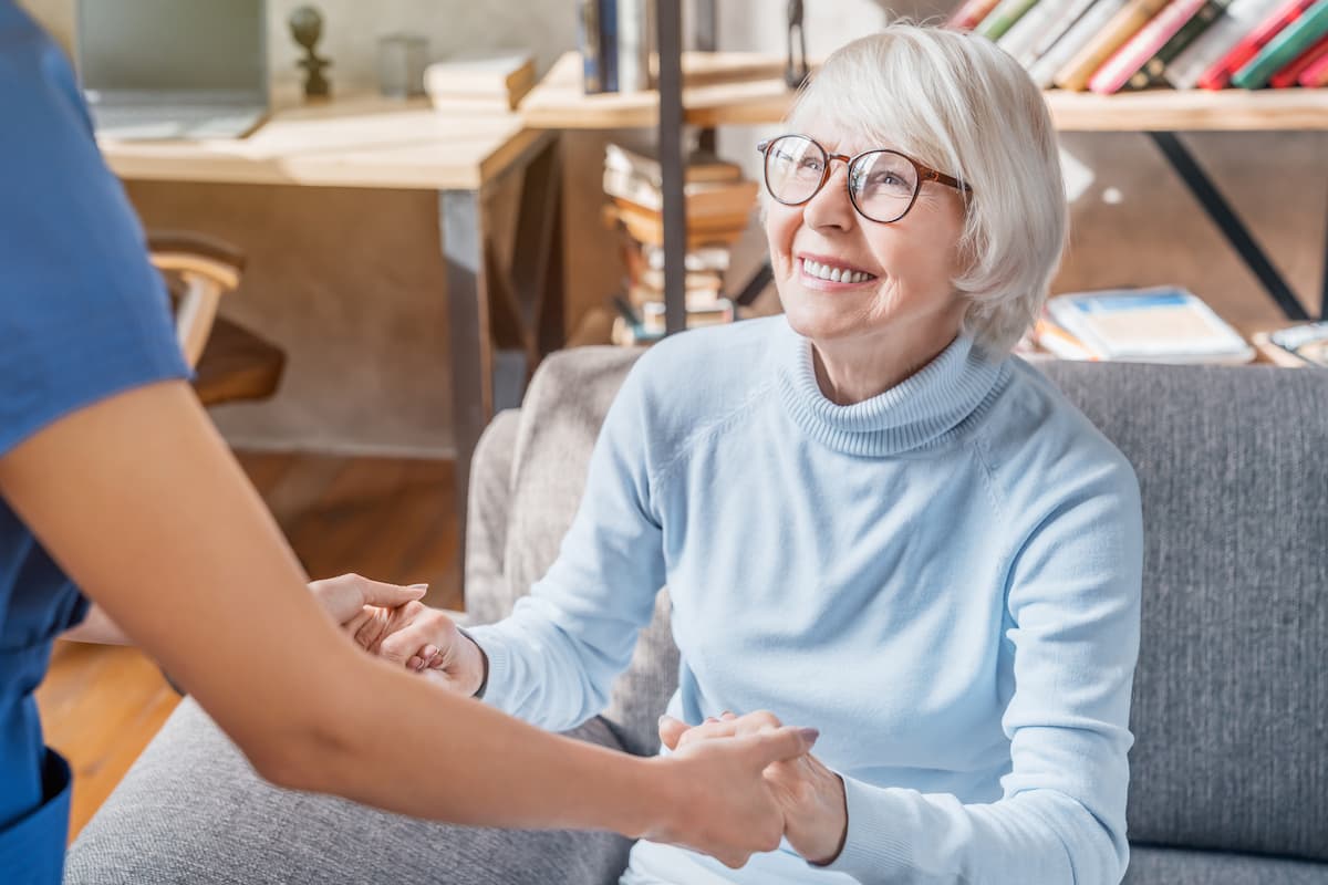 female resident looking up and smiling at caregiver while holding her hands