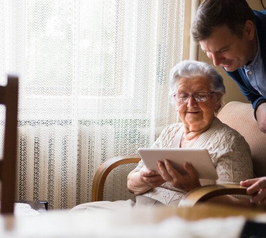 Mature woman using digital tablet in front of her adult grandson.