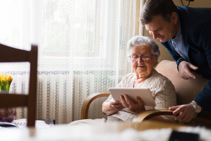 Mature woman using digital tablet in front of her adult grandson.