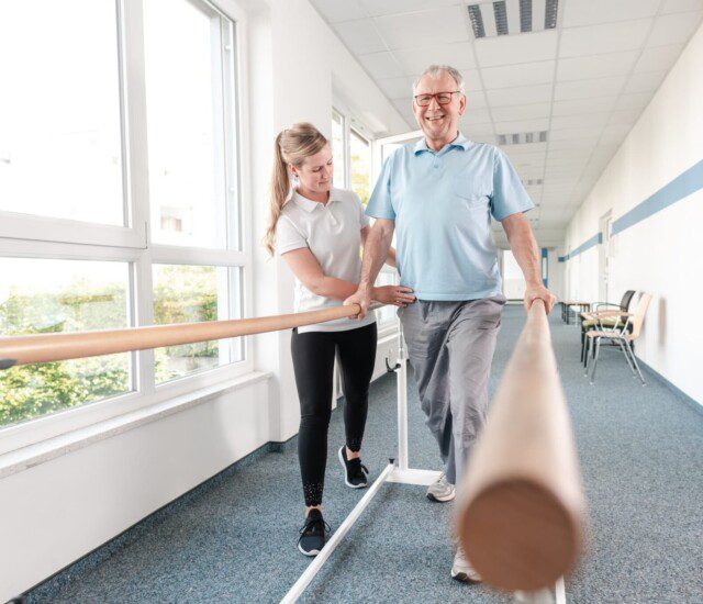 caregiver helping resident with physical therapy on the parallel bars