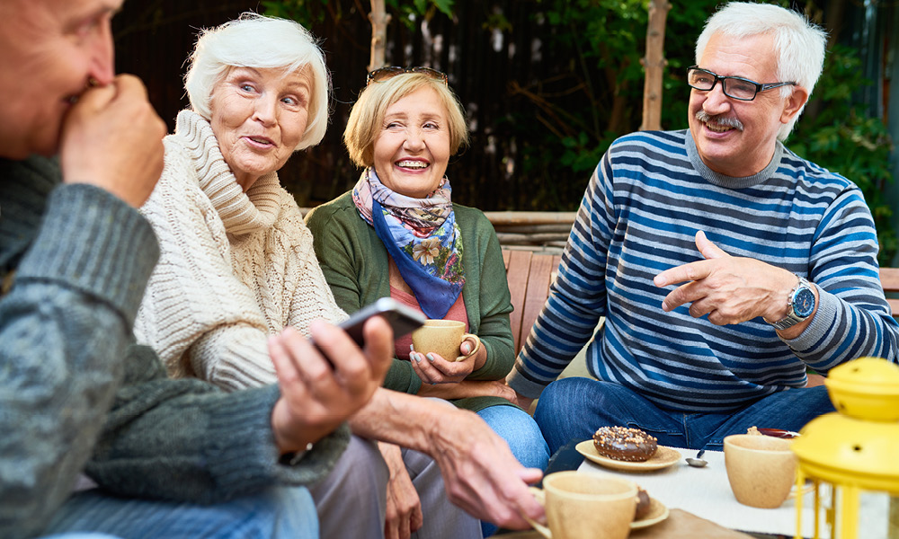 Double date of elderly couple having coffee outdoors.