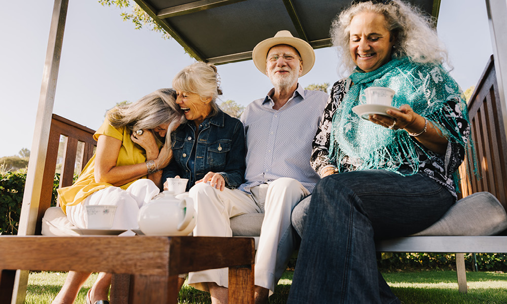 group of elderly smiling while having tea outside.