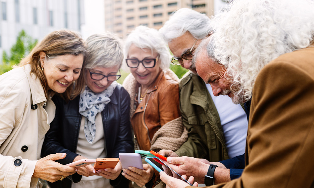Group of elderly all looking down and smiling at their phones.