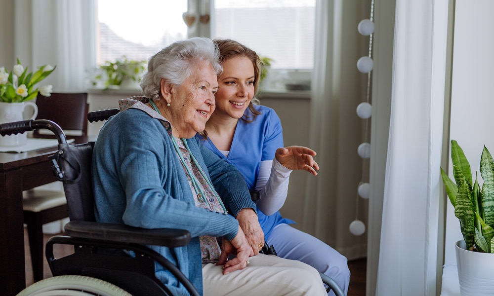 Nurse smiling while talking with an elderly lady in a wheel chair.