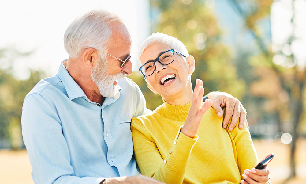 smiling senior couple sitting out doors at a park while talking.