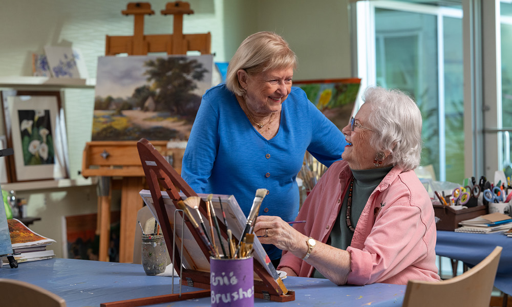 Two elderly ladies smiling while painting together.