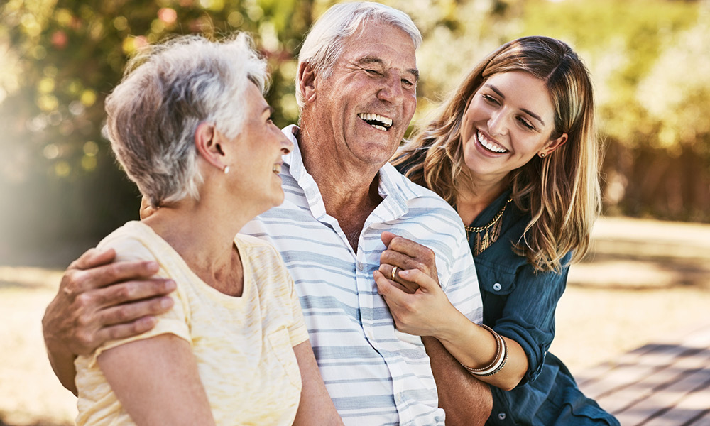 Elderly parents laughing with their daughter while sitting on a bench.